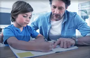 Adult helping child with homework at table.